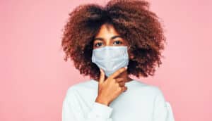 A young woman wearing a face mask looks inquisitive and puts her hand to her chin.