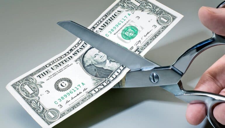 A person uses scissors to cut a dollar bill in half.