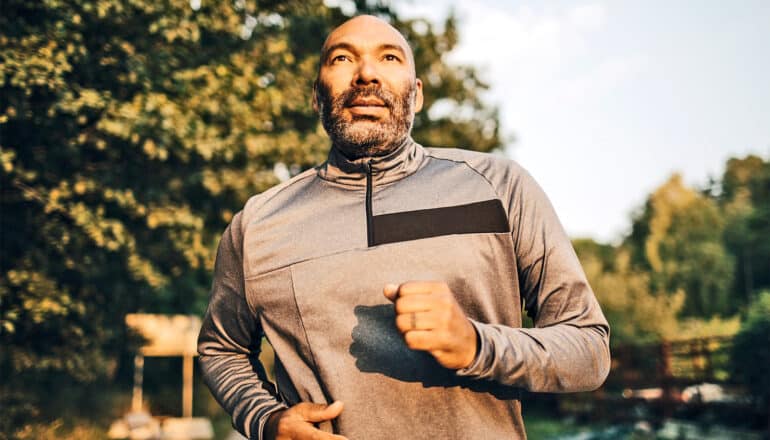 A man jogs in a park while looking slightly upwards.