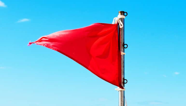A triangular red flag waves against a bright blue sky.