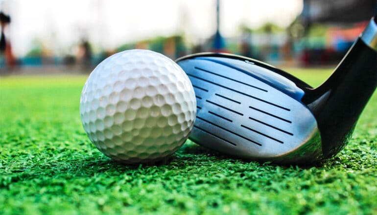 A golf ball sits on artificial grass next to a club.