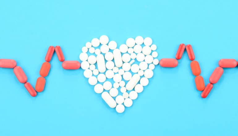 A heart shape made out of white pills with a heart beat monitor shape made of red pills on either side of it.