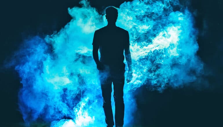 A man walks through a cloud of bright blue smoke in silhouette.