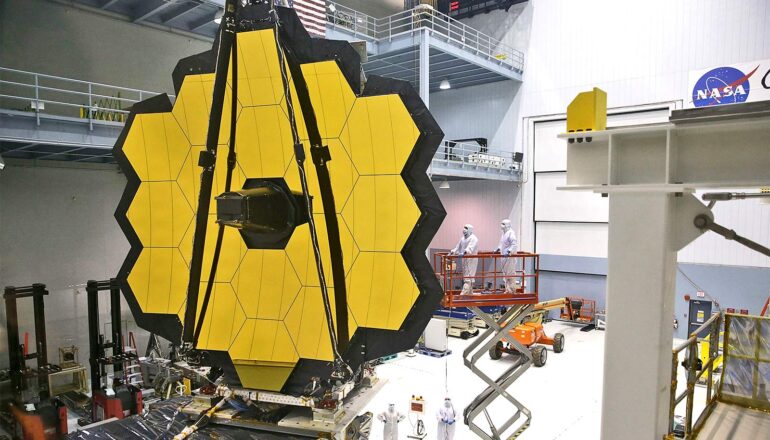 Scientists in white sterile gear work on the gigantic honeycomb-shaped telescope in a large hanger.