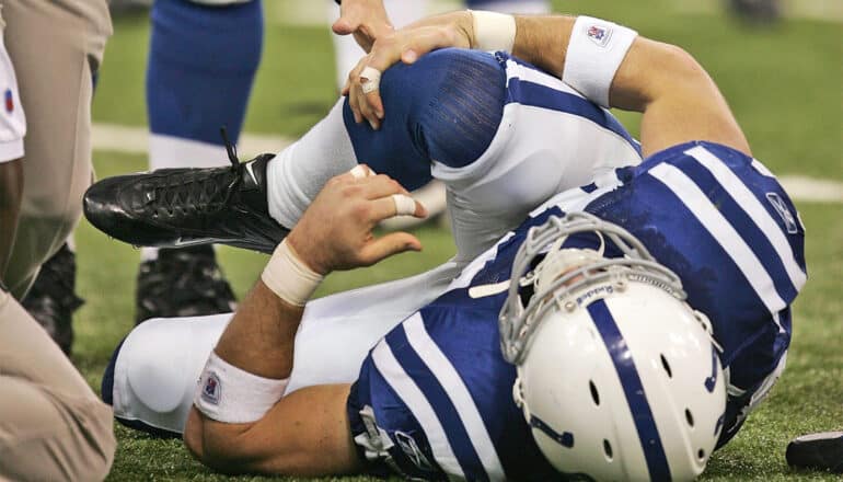 An NFL player lays on his back on the field and clutches his right knee.