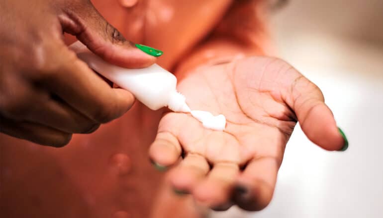 A woman with green nails squeezes a white bottle of lotion into one hand.