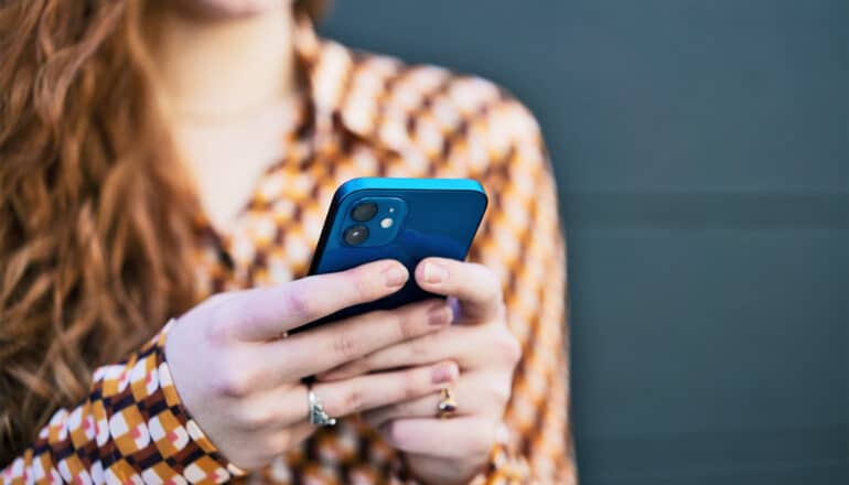 A woman reads her phone while standing outside.