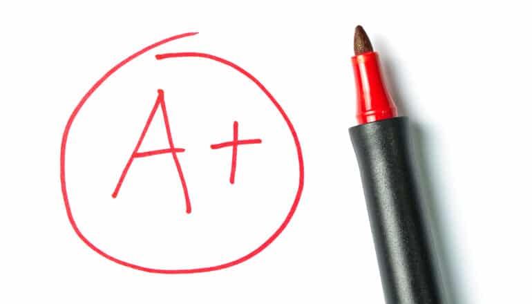 A red pen sits on white paper next to a handwritten "A+" in a red circle.