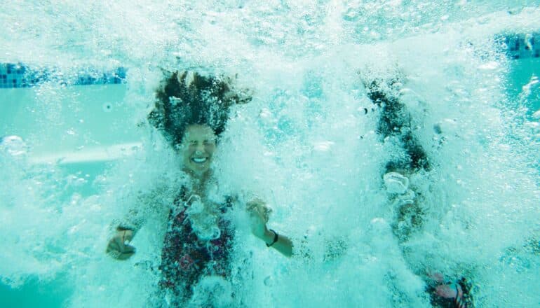 A woman smiles underwater after just jumping into a pool with a friend.