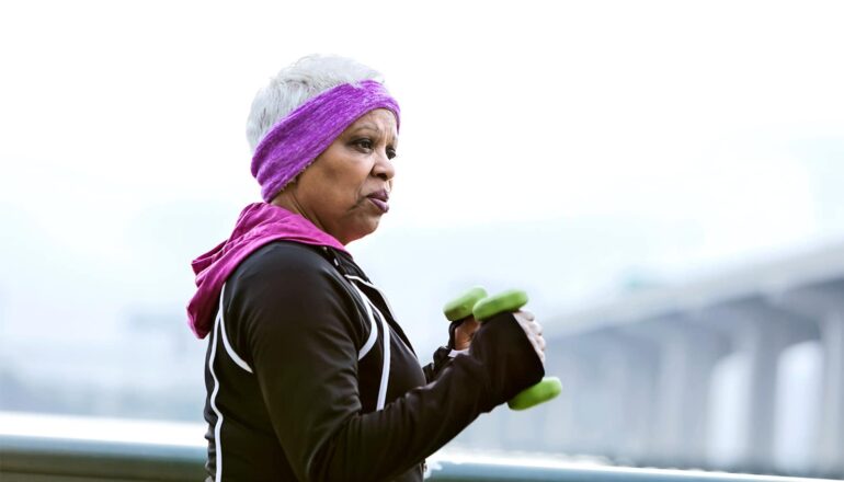 A woman walks outside while carrying weights in each hand.