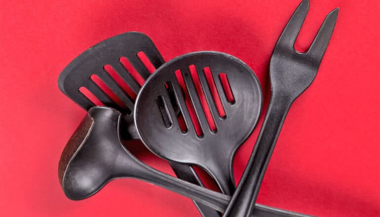 Black plastic kitchen utensils sit on a red surface.