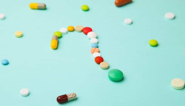 Differently colored pills arranged in the shape of a question mark.
