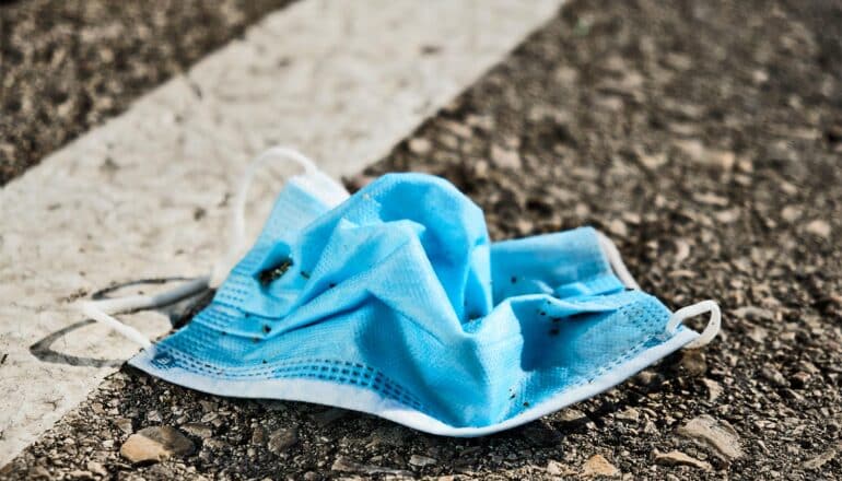 A crumpled blue surgical mask sits on an asphalt street.