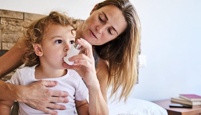 A mother helps her young child with an asthma inhaler.