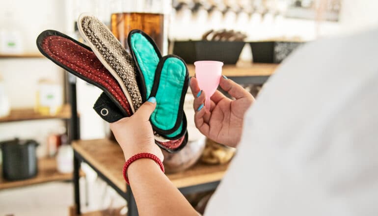 A woman examines several reusable pads and a menstrual cup in a store.