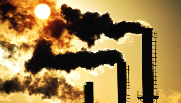 Black smoke pours out of three smokestacks at sunset.
