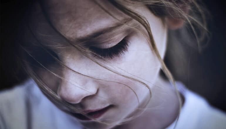 A young girl looks downward, away from the camera.