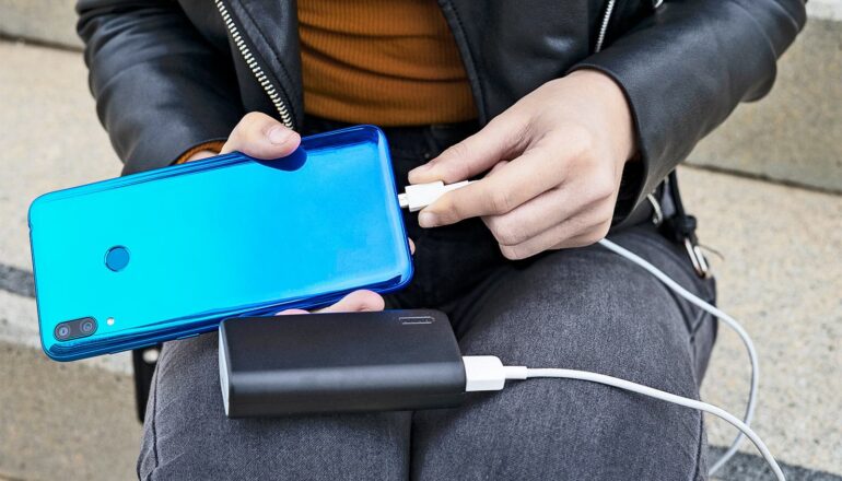 A person plugs their phone into a portable battery to charge it.