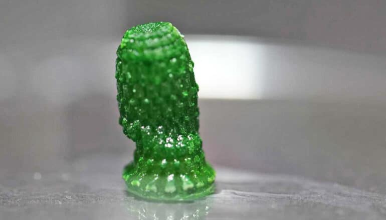 A small, green pineapple shaped structure stands upright on a metal surface.