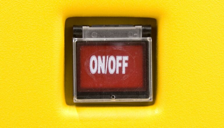 A red on/off switch under a plastic cover on a yellow wall.
