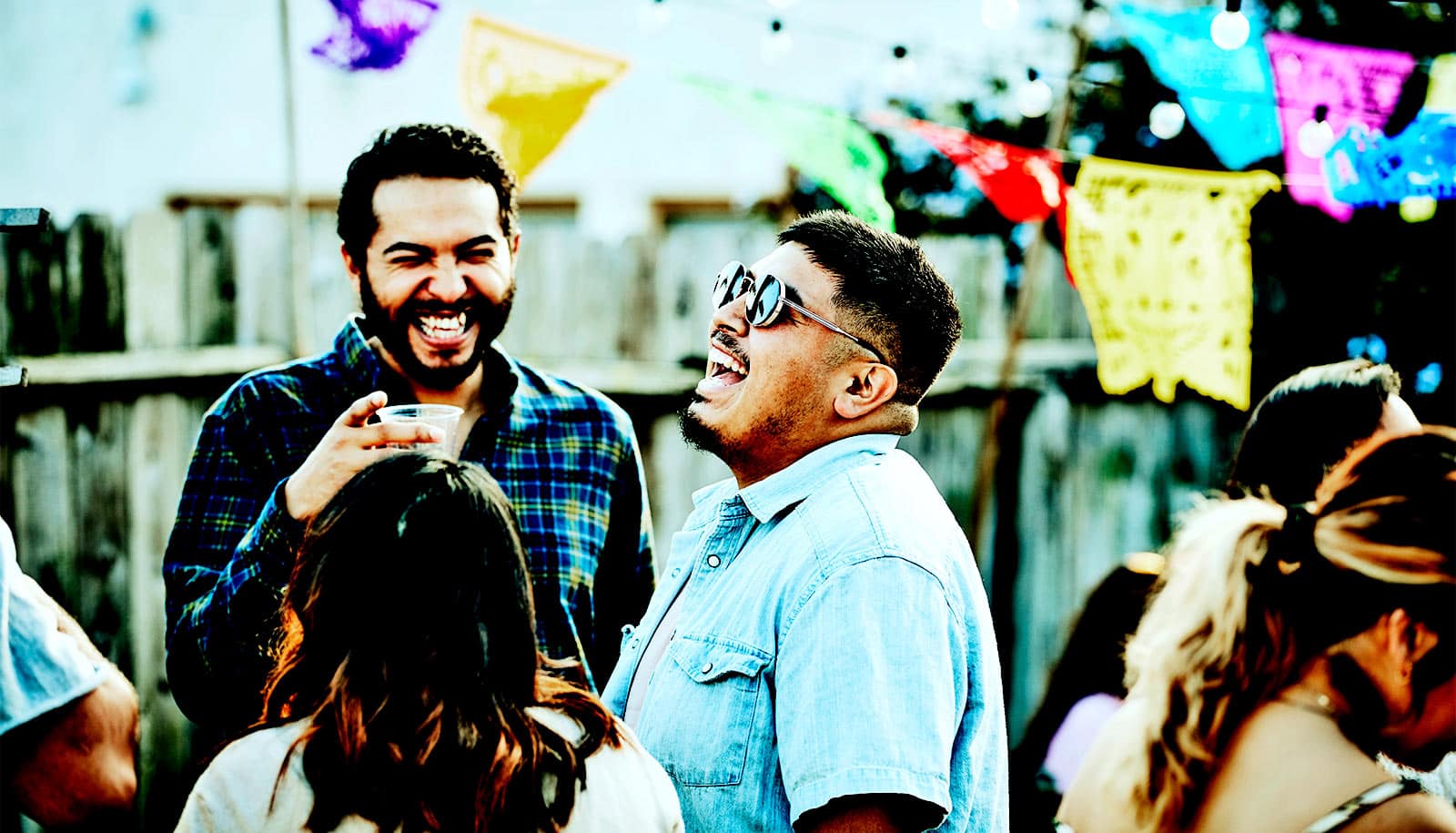 A group of friends laugh together outside at a backyard party.