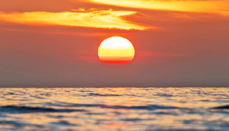 The sun sets over a body of water.
