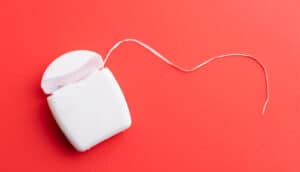 A white package of dental floss on a red surface.