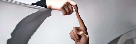 Two human fingers touch over a sheet of fabric separating them.