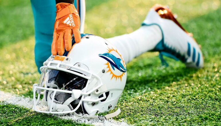 A football player from the Miami Dolphins kneels with one hand on his helmet.