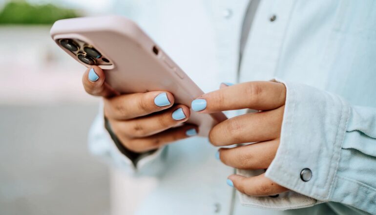 A young woman with blue nails looks at her phone.