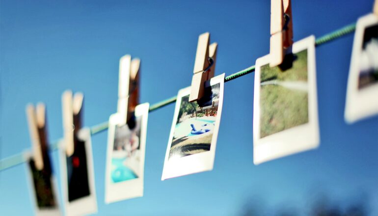 Photographs hang on a wire outside, clipped to it with clothing pins.
