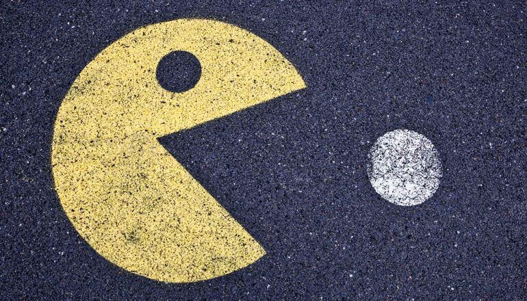 A yellow Pac-Man character is painted eating a white circle on black asphalt.