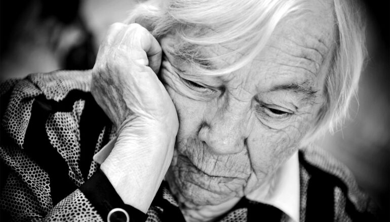 An older woman looks down as she rests her head on her hand.