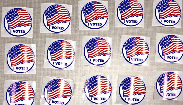 Rows of "I voted" stickers with American flags on them sit in rows on a wall.