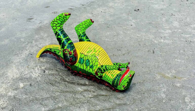 A toy dinosaur lies on cement on its back as if dead.
