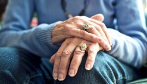 An older woman holds both hands together over her knee.