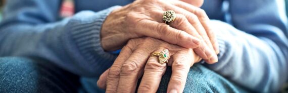 An older woman holds both hands together over her knee.