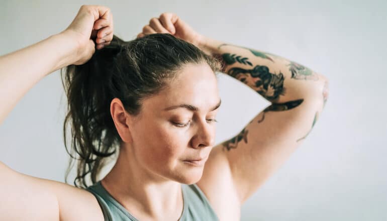 A woman with a few tattoos on her left arm puts her hair up.