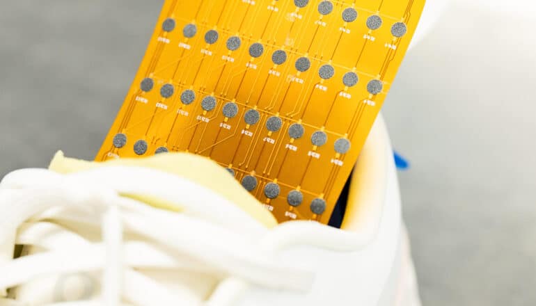 The gold-colored shoe insert, covered in electronic nodes, sits in a white tennis shoe.