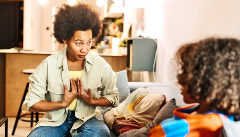 A mother speaks with her teenage son while gesturing to herself with both hands.