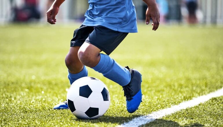 A young teen plays soccer on a field.