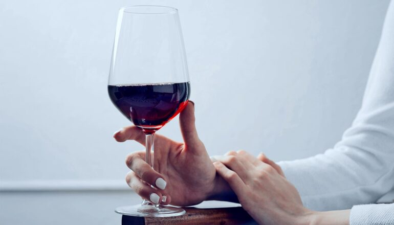 A woman holds a glass of red wine on a table.