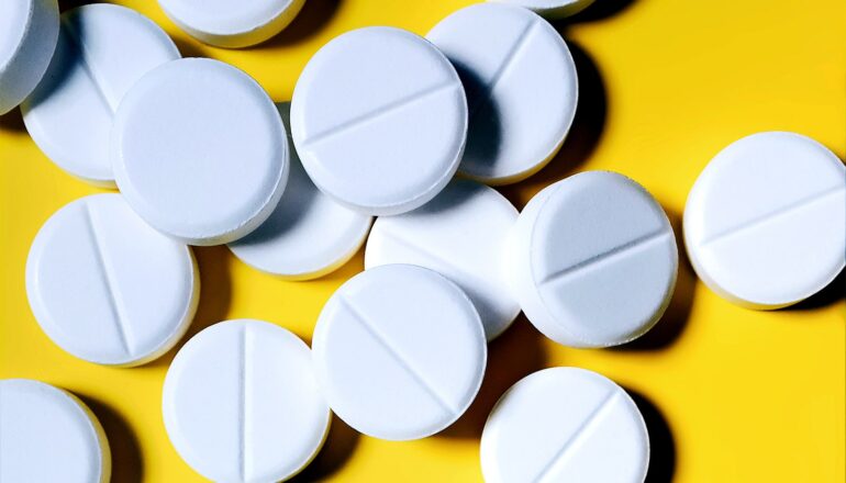 Many white pills on a yellow background.