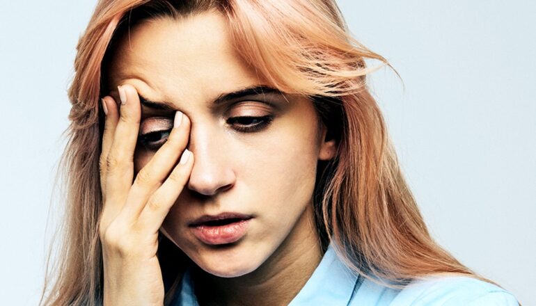A young woman looks distressed as she puts one hand over her right eye.