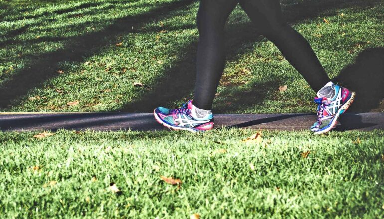 A person runs outside on a path surrounded by grass.