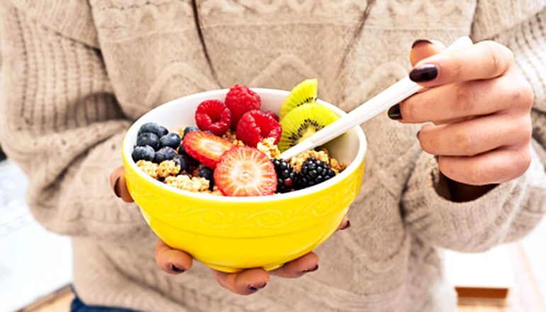 A woman holds a bowl of grains and fruit.