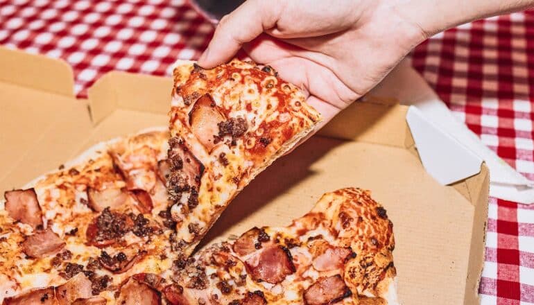 A person grabs a slice of pizza from a box.