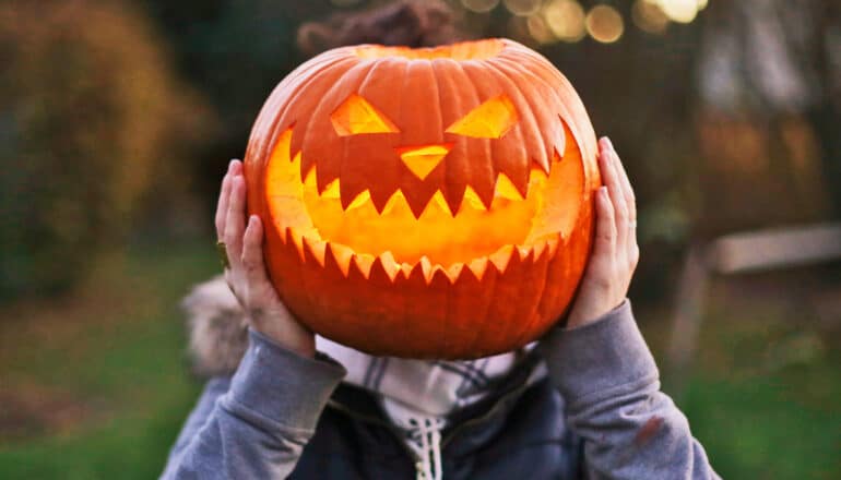 A person holds a Jack-o-lantern in front of their face.