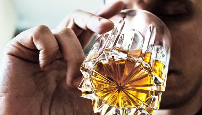 A man sips brown liquor from a glass.