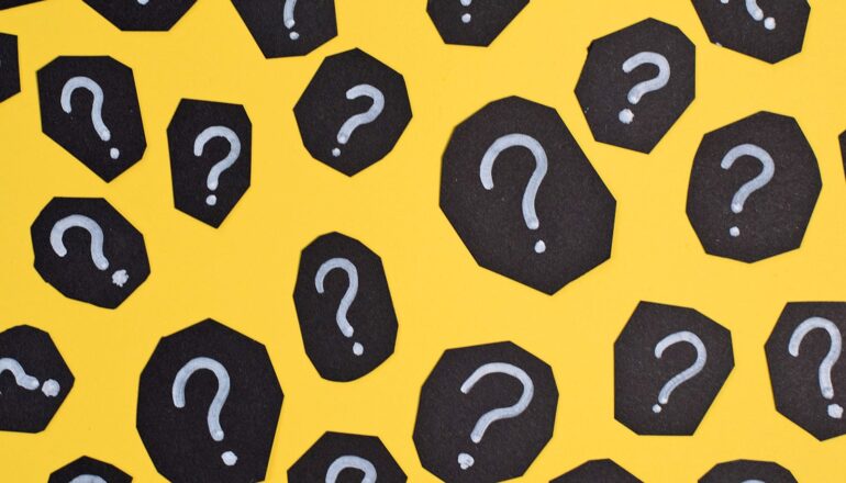 Many black pieces of paper on a yellow background with white question marks on them.